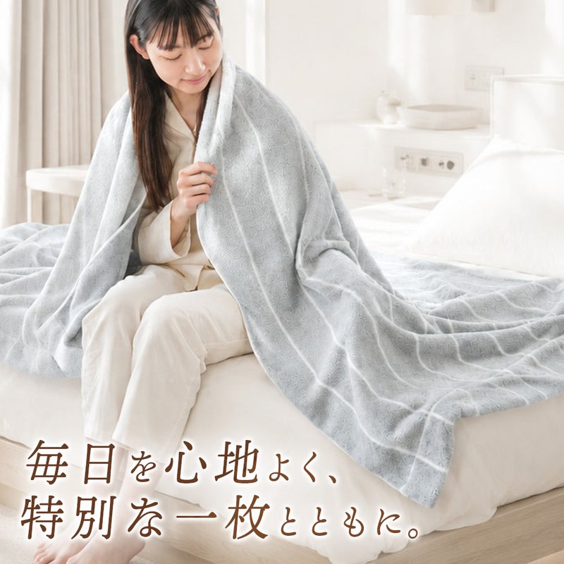 ベッドに腰掛け、グレーの今治タオルケットを優しく肩から羽織る笑顔の女性。「毎日を心地よく、特別な一枚とともに。」オーガニックコットン100%の日本製シングルタオルケット。ねごこち本舗